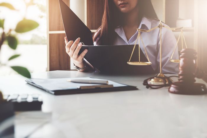 Eine Frau im Anzug hält einen Ordner und eine Justitia-Waage, symbolisiert rechtliche Expertise als Notarin.